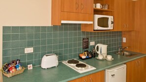 Une cuisine compacte avec des meubles en bois, un four à micro-ondes, un grille-pain, une bouilloire et un petit évier.