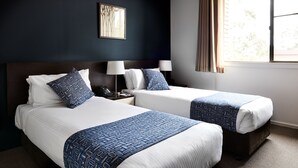Une chambre d’hôtel avec deux lits, une table de chevet avec un téléphone, une lampe et un tableau encadré au mur.