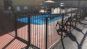 A fenced pool area with a blue pool, a red deck, and a white car parked nearby. - Smoky View Inn (Pigeon Forge)