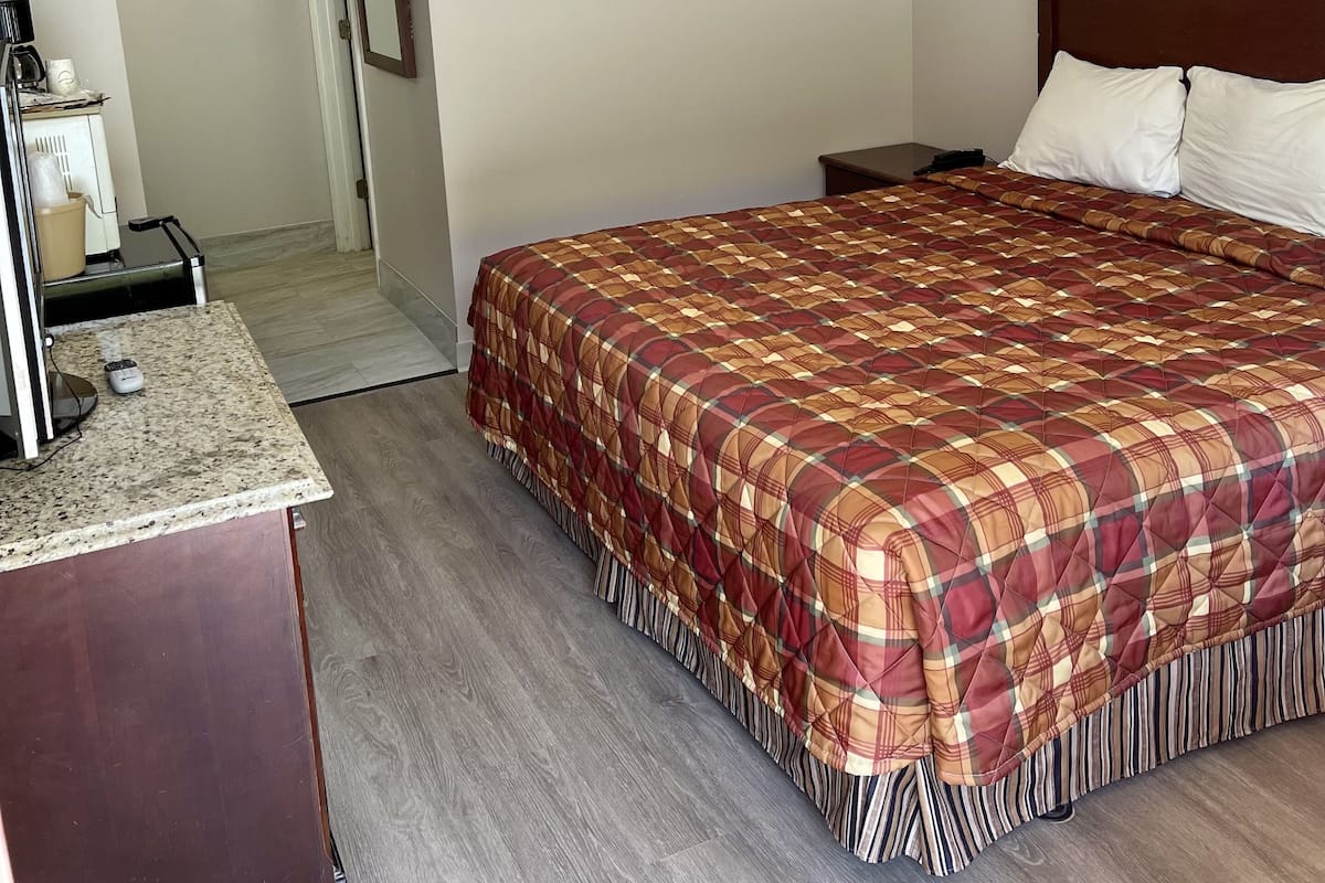Hotellihuone, jossa on suuri sänky, puinen pääty, yöpöytä, työpöytä lampun kanssa ja ovi, joka johtaa toiseen huoneeseen.