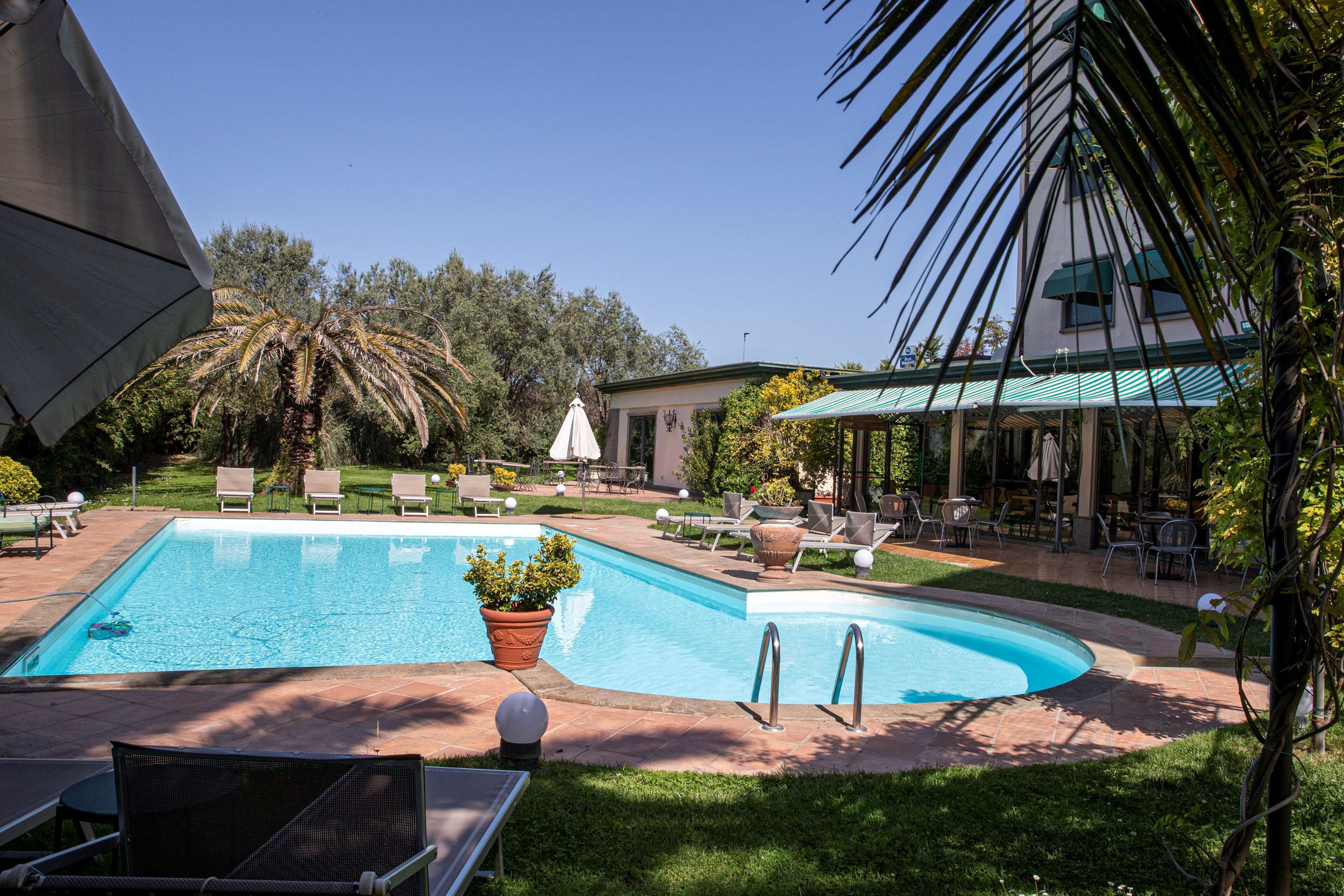 Une piscine rectangulaire à bords incurvés, entourée d’un espace patio aménagé avec des chaises longues et des tables.