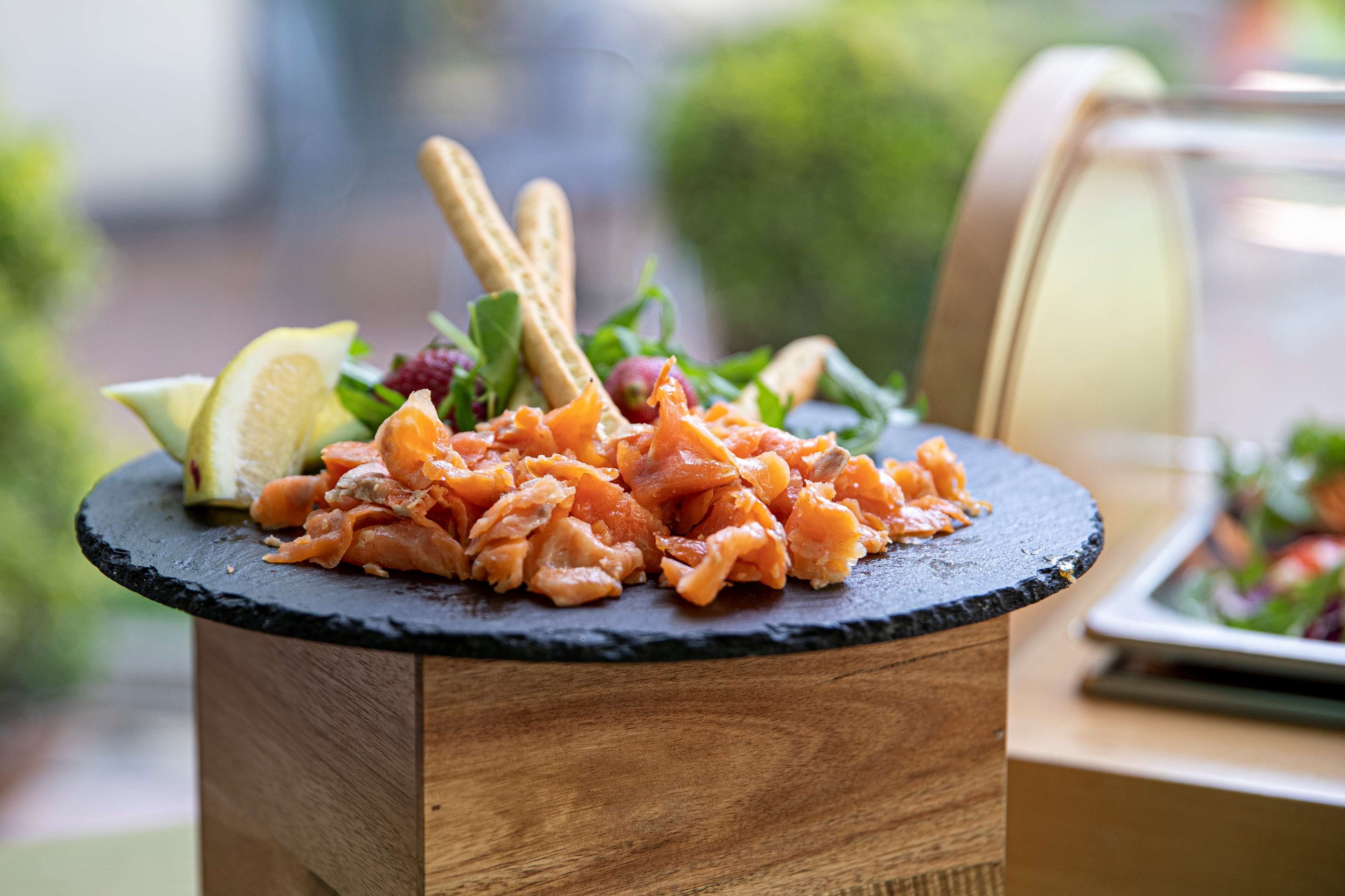 A meal with salmon, lemon, and greens on a slate plate.