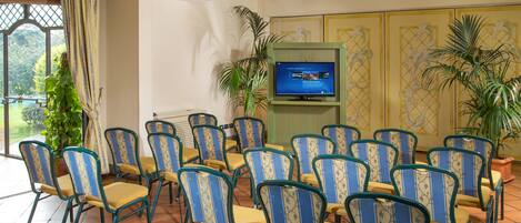 A conference room with multiple chairs arranged in rows, a television screen, and potted plants.