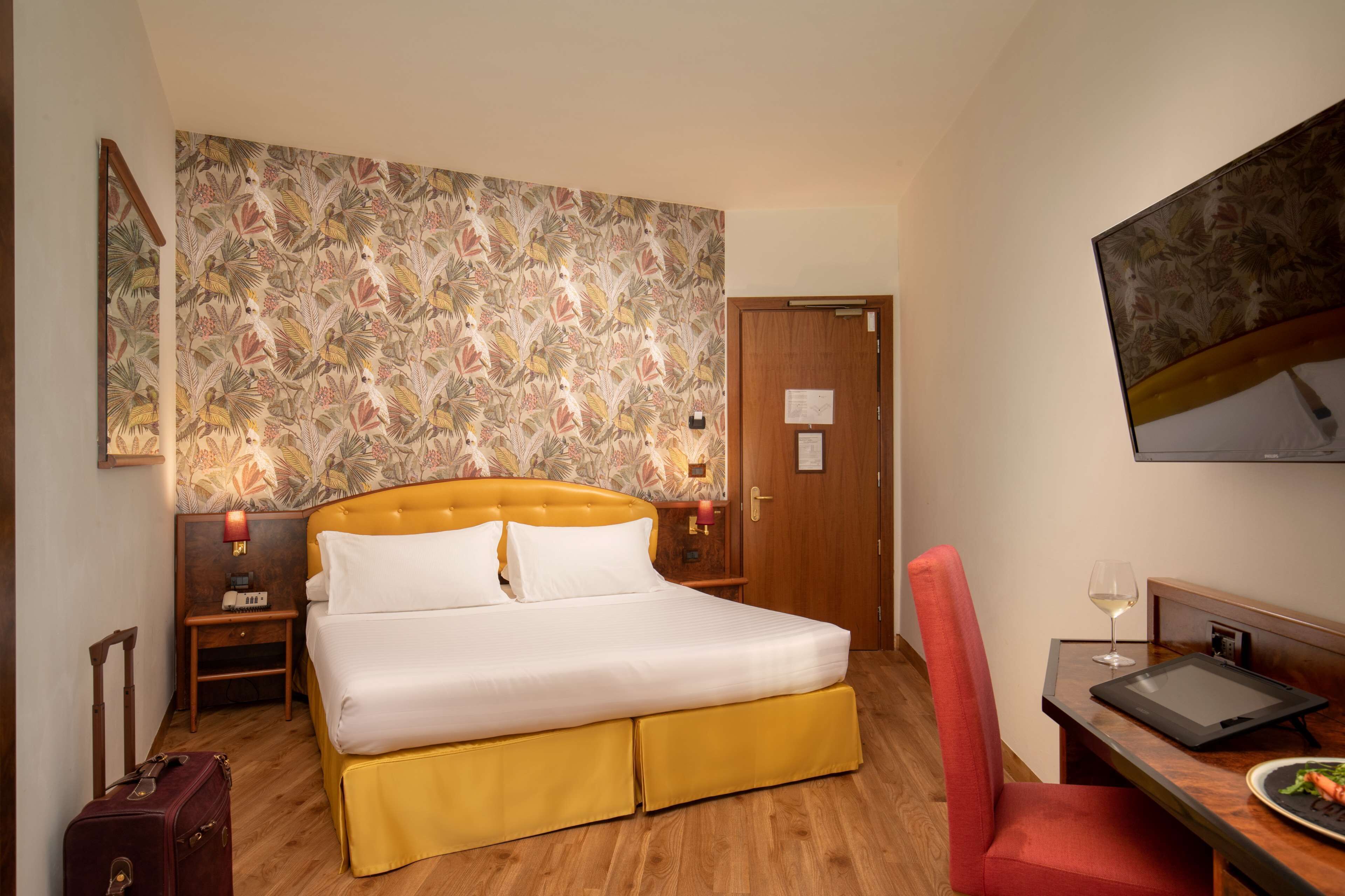 A hotel room with a bed, a desk, a chair, a suitcase, and a television.