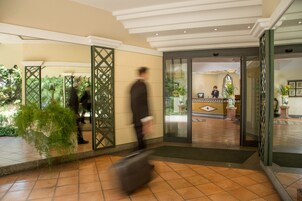 Un vestíbulo de hotel con una recepción, una planta grande en maceta y un suelo de baldosas.