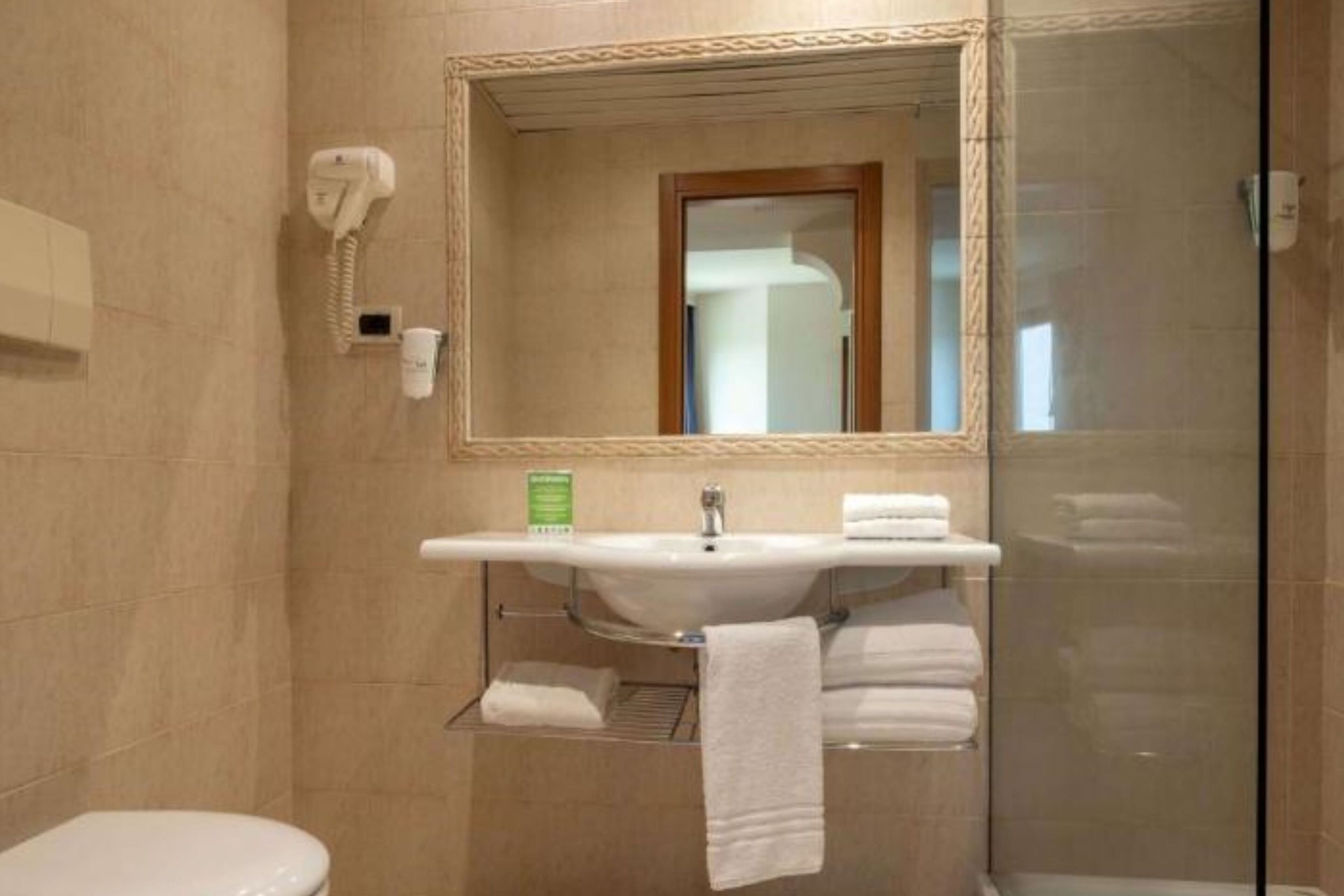Une salle de bain équipée d’un lavabo, d’un miroir, d’un porte-serviettes et d’une cabine de douche en verre.