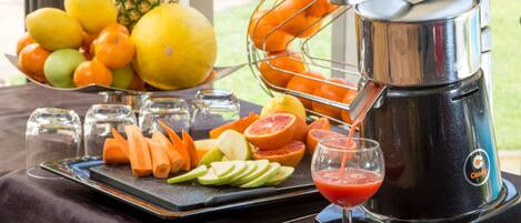 A juicer with a tray of sliced fruits and a glass of juice.