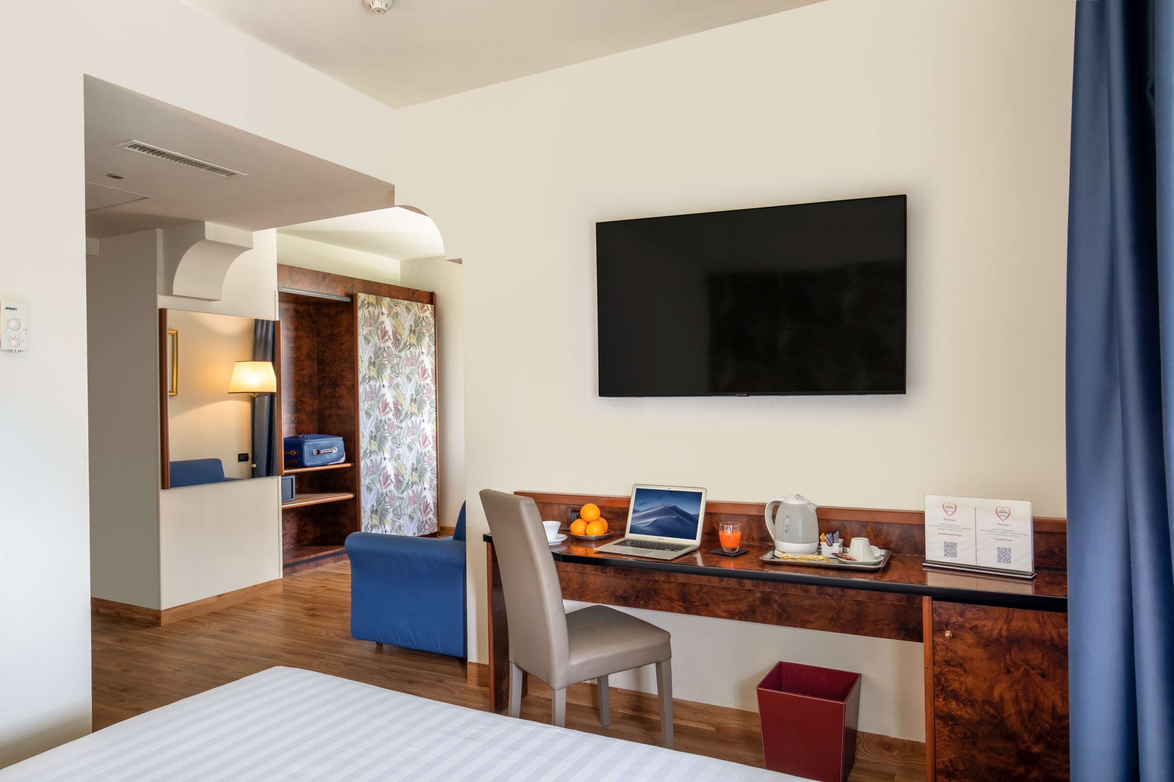 Habitació d'hotel amb un llit, una taula de treball amb un ordinador portàtil, un televisor de pantalla plana, una cafetera i un petit cendrer.
