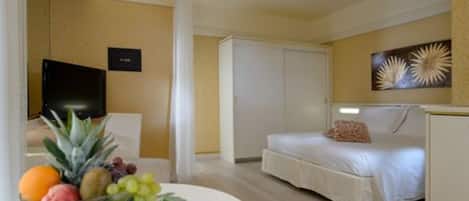 Une chambre d’hôtel avec un lit, une télévision, un panier de fruits sur une table et un tableau au mur.