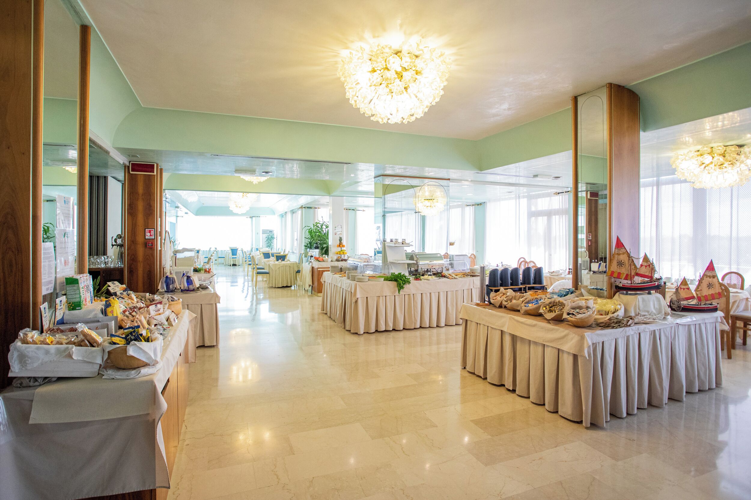 Ein geräumiger Festsaal mit mehreren Tischen, die für ein Buffet gedeckt sind, großen Kronleuchtern und einem hellen, gut beleuchteten Innenraum.
