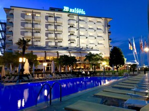 A hotel with a pool area, multiple balconies, and flags.