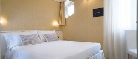 Una habitación de hotel con una cama grande, una mesita de noche, una silla y un ventanal con cortinas.