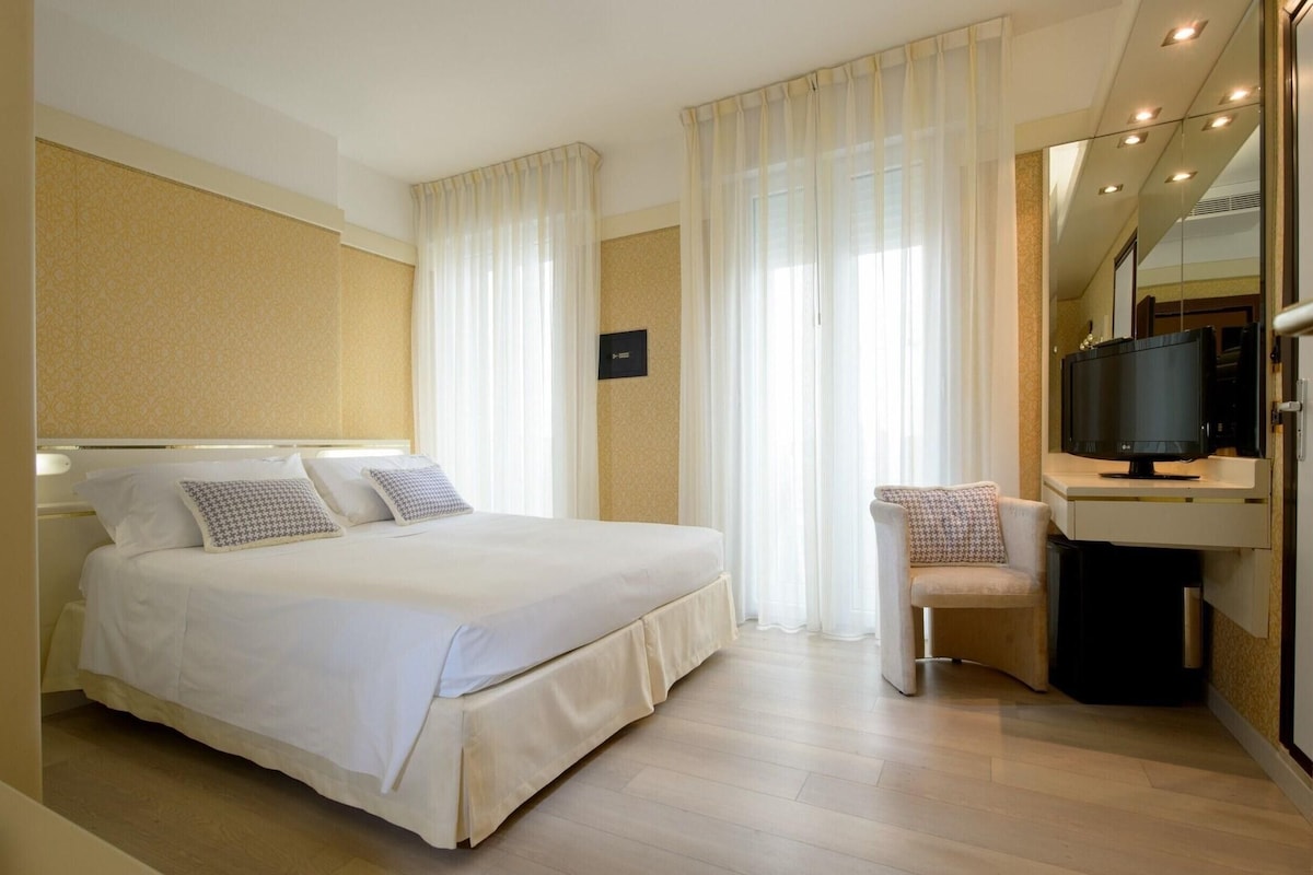 A hotel room with a bed, a chair, a desk with a television, and a mirror.