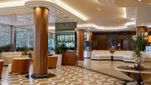 A spacious lobby with a checkered floor, large wooden columns, a white sofa, and a reception desk. - Hotel Bristol (Chioggia)
