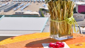 A glass vase with white flowers and dried reeds on a table with a beach view in the background. - Hotel Bristol (Chioggia)