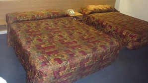 Ein Hotelzimmer mit zwei Betten, jedes mit einer gemusterten Tagesdecke, einem Nachttisch mit Telefon und Wandleuchten.