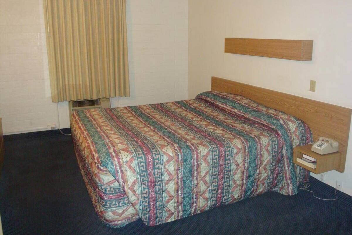 A standard hotel room with a single bed, a bedside telephone, and a small bedside table.