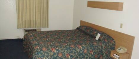 A single bed with a floral bedspread, a bedside telephone, and a small shelf with books.