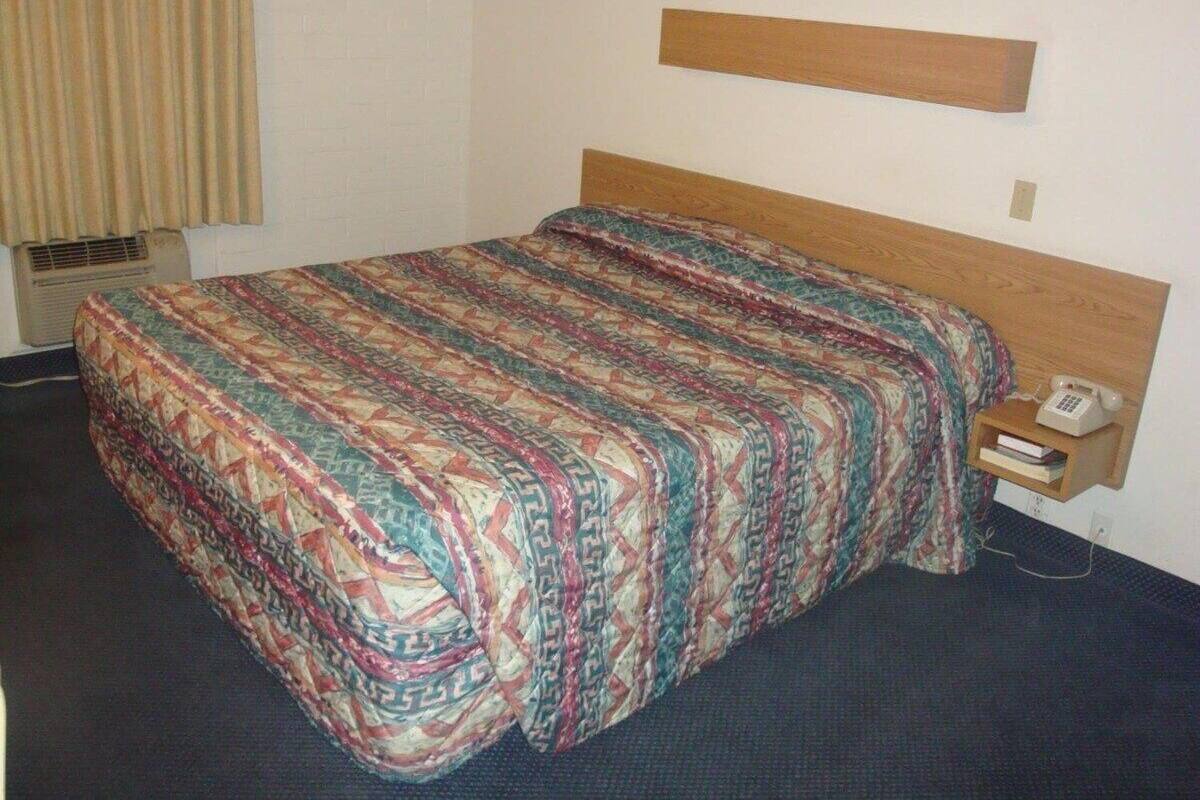 A hotel room with a bed, a telephone, and a shelf with a book.