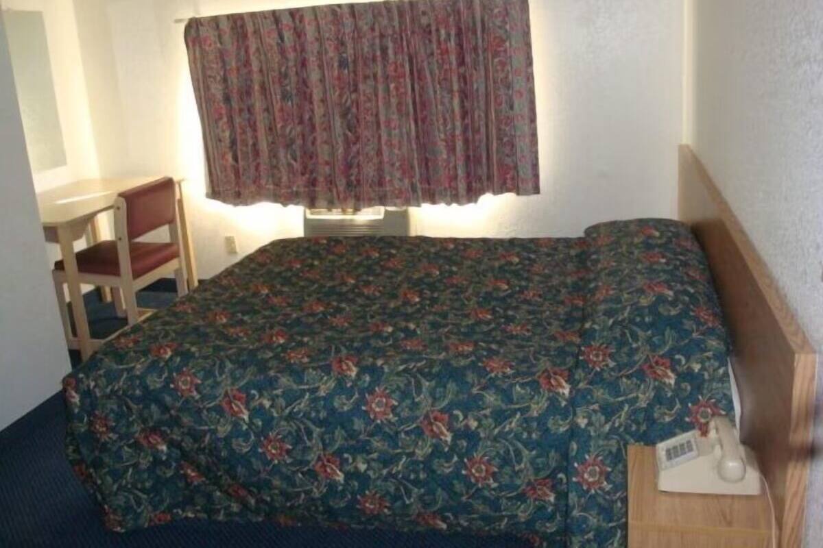 A small, single-bed room with a floral bedspread, a wooden nightstand, a chair, and a desk.
