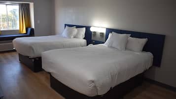 Two beds with white bedding in a room with a window and a wall-mounted light.