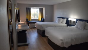 Ett hotellrum med två sängar, ett skrivbord, en stol, ett fönster med gardiner och en tv.