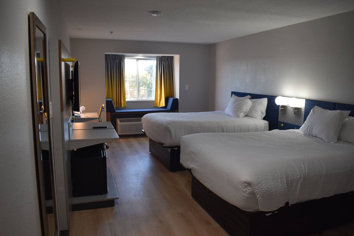 Une chambre d’hôtel avec deux lits, un bureau, une chaise, une fenêtre avec des rideaux et un téléviseur.