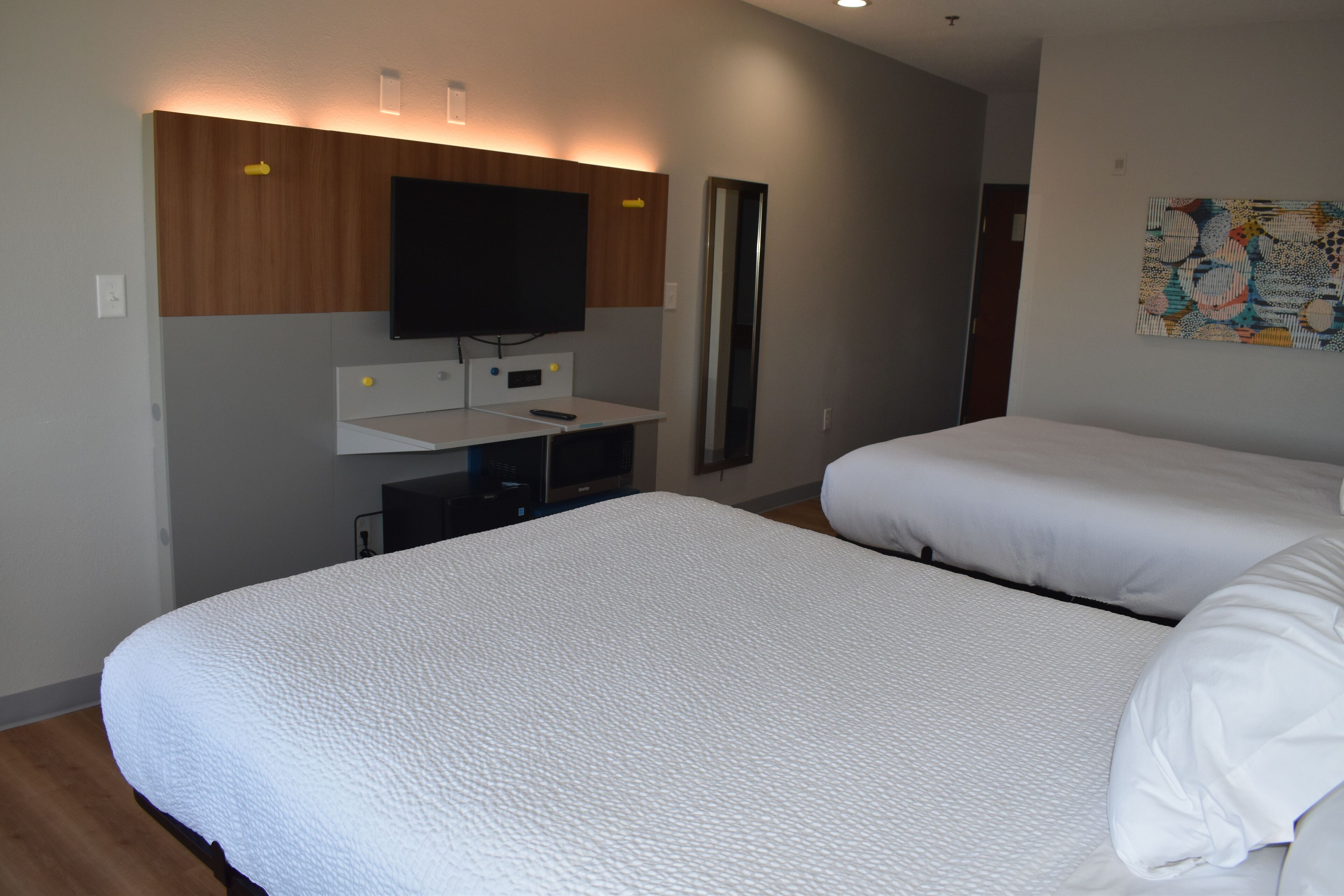 A hotel room with two beds, a flat-screen TV mounted on the wall, a small desk with a chair, and a painting on the wall.