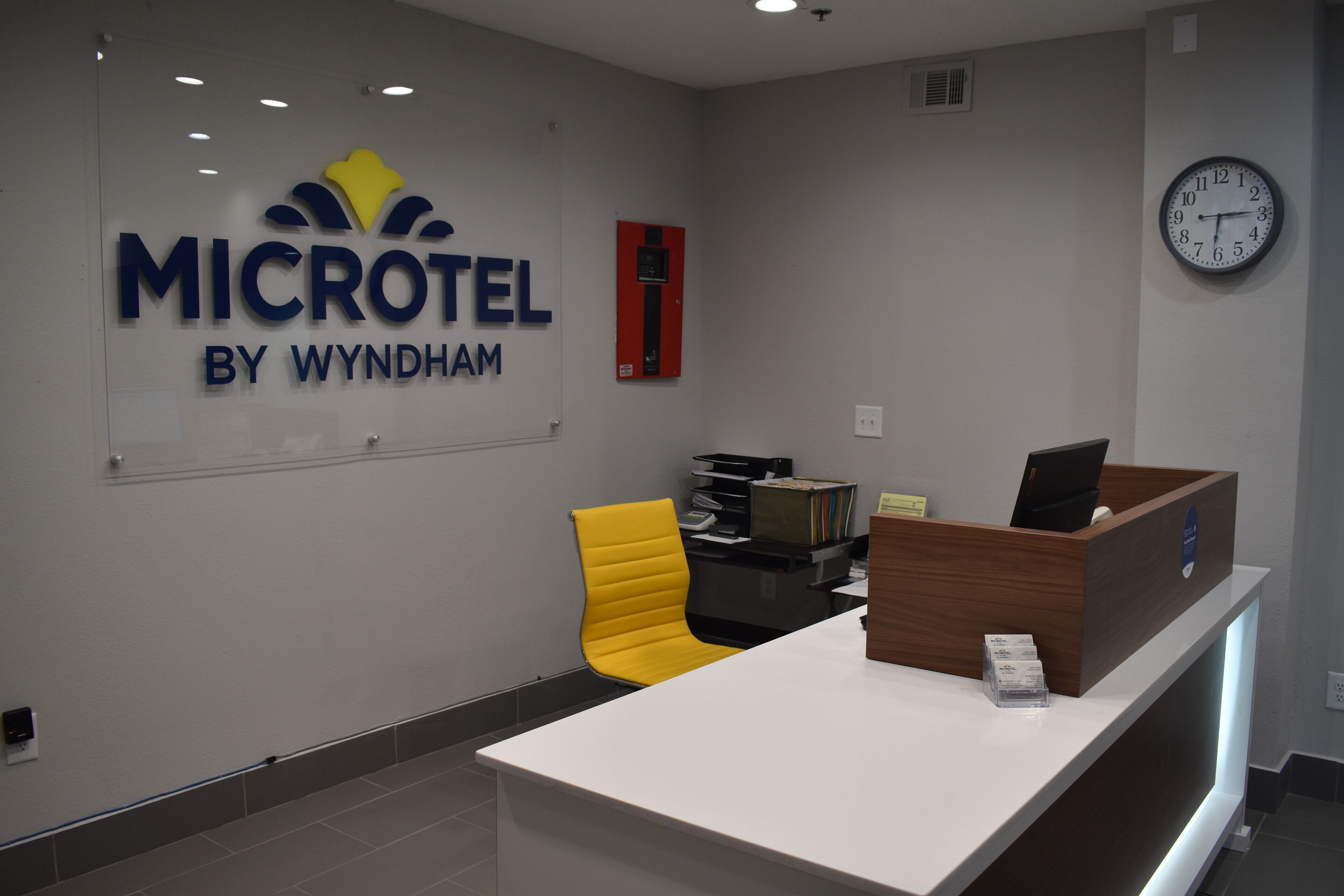 A reception desk with a sign reading "MICROTEL BY WYNDHAM," a clock, and a yellow chair.