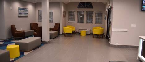 A modern lobby with seating areas, a reception desk, and a large window with blinds.
