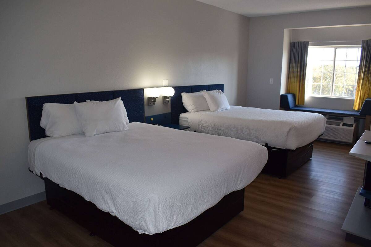 Une chambre d’hôtel avec deux lits, un bureau et une fenêtre avec des rideaux.