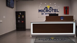 En receptionsdisk med träinredning och en digital display, en brandsläckare som är monterad på väggen och en hylla med diverse föremål.