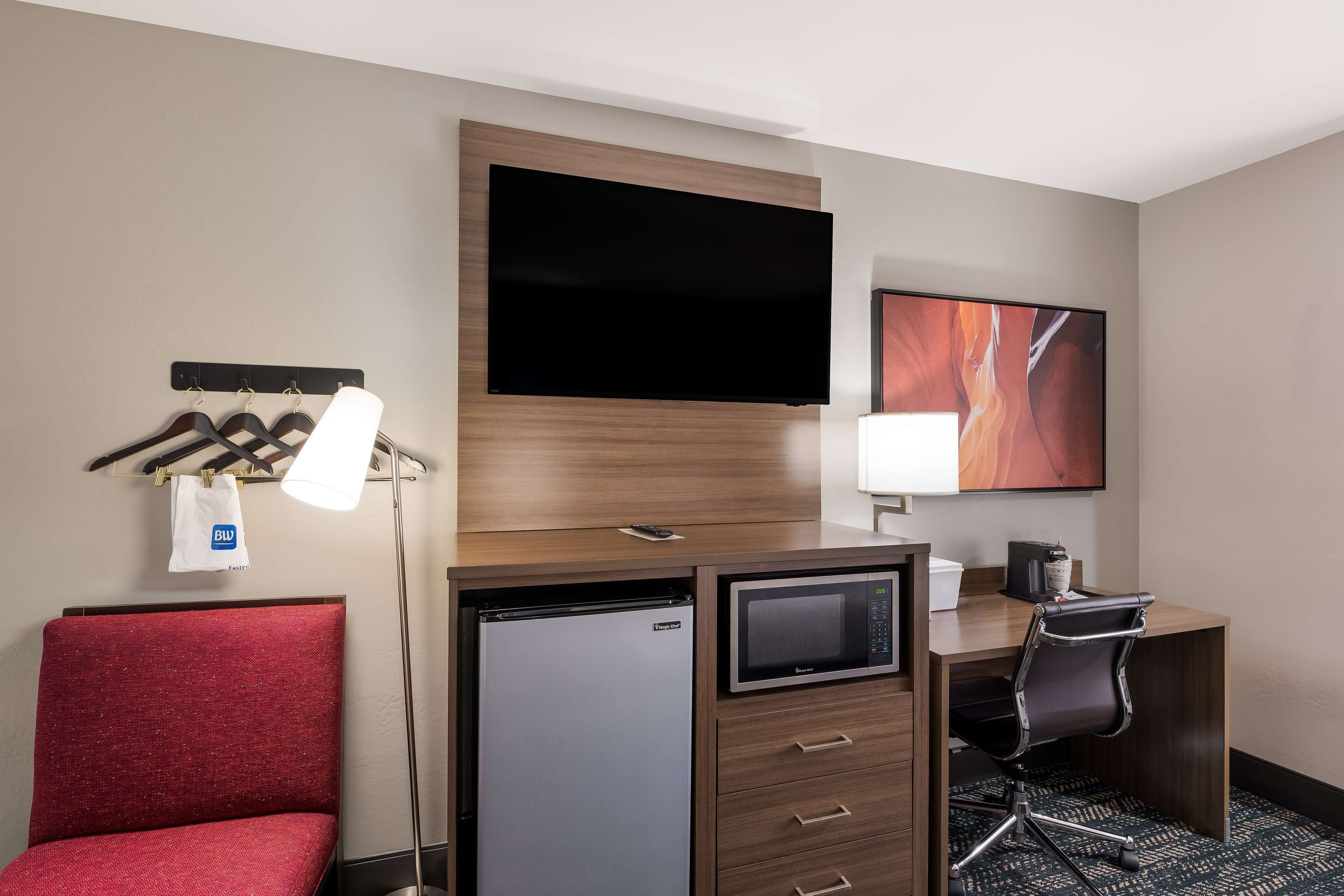 Quarto de hotel com cama, escrivaninha com computador, televisão, frigorífico e micro-ondas.