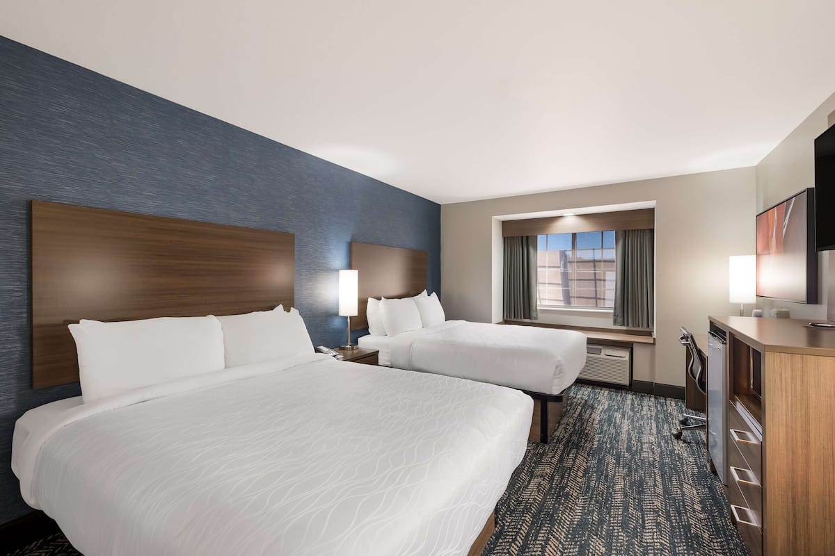 A hotel room with two beds, a desk, a television, and a window with curtains.