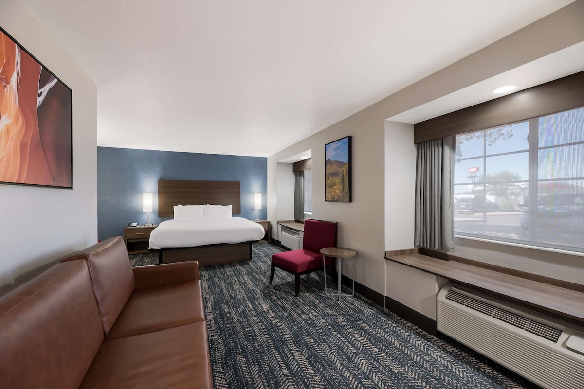 A hotel room with a bed, a red chair, a small table, and a large window.