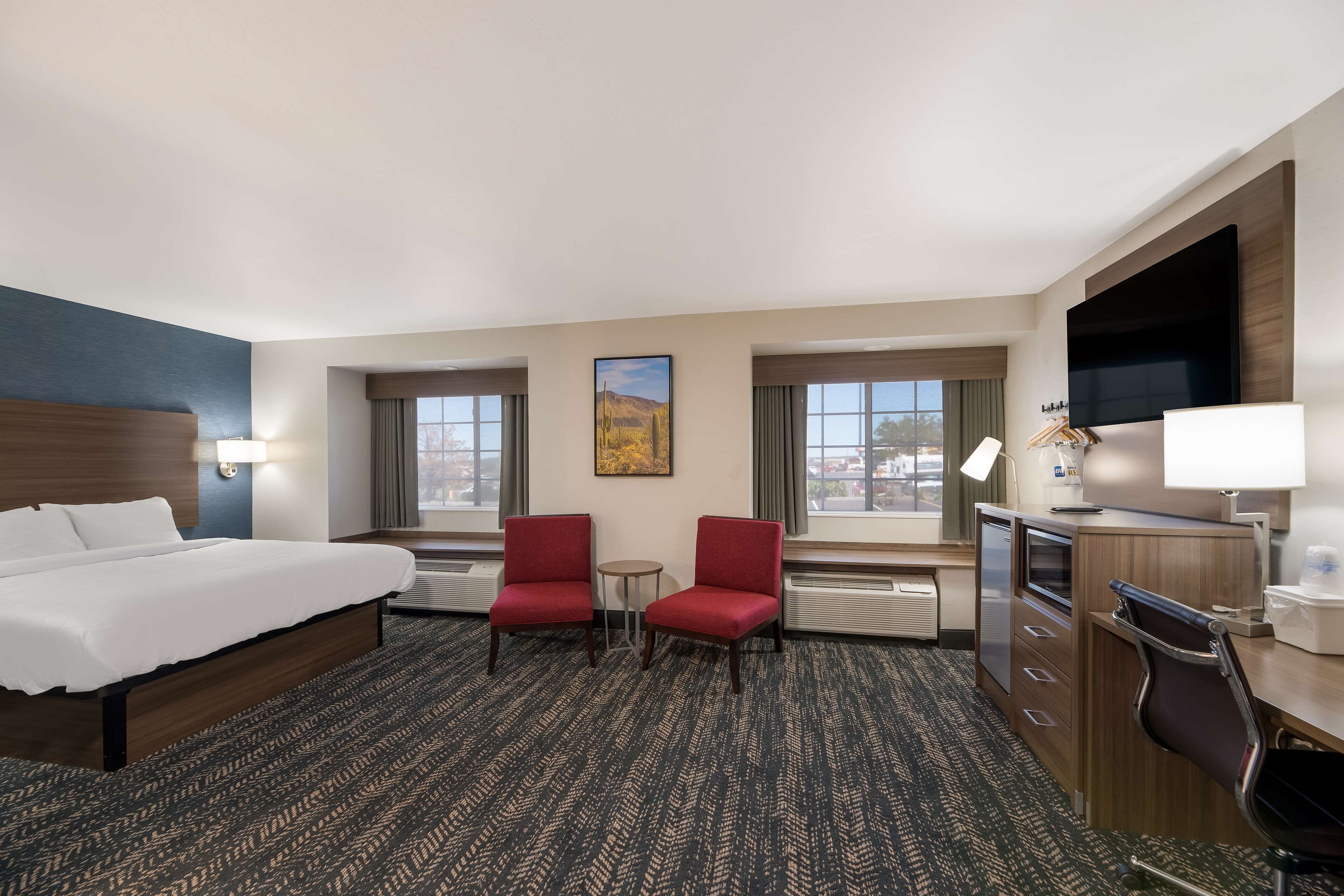 A hotel room with a bed, two red chairs, a desk, a TV, and a painting on the wall.