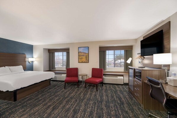 A hotel room with a bed, two red chairs, a desk, a TV, and a painting on the wall.