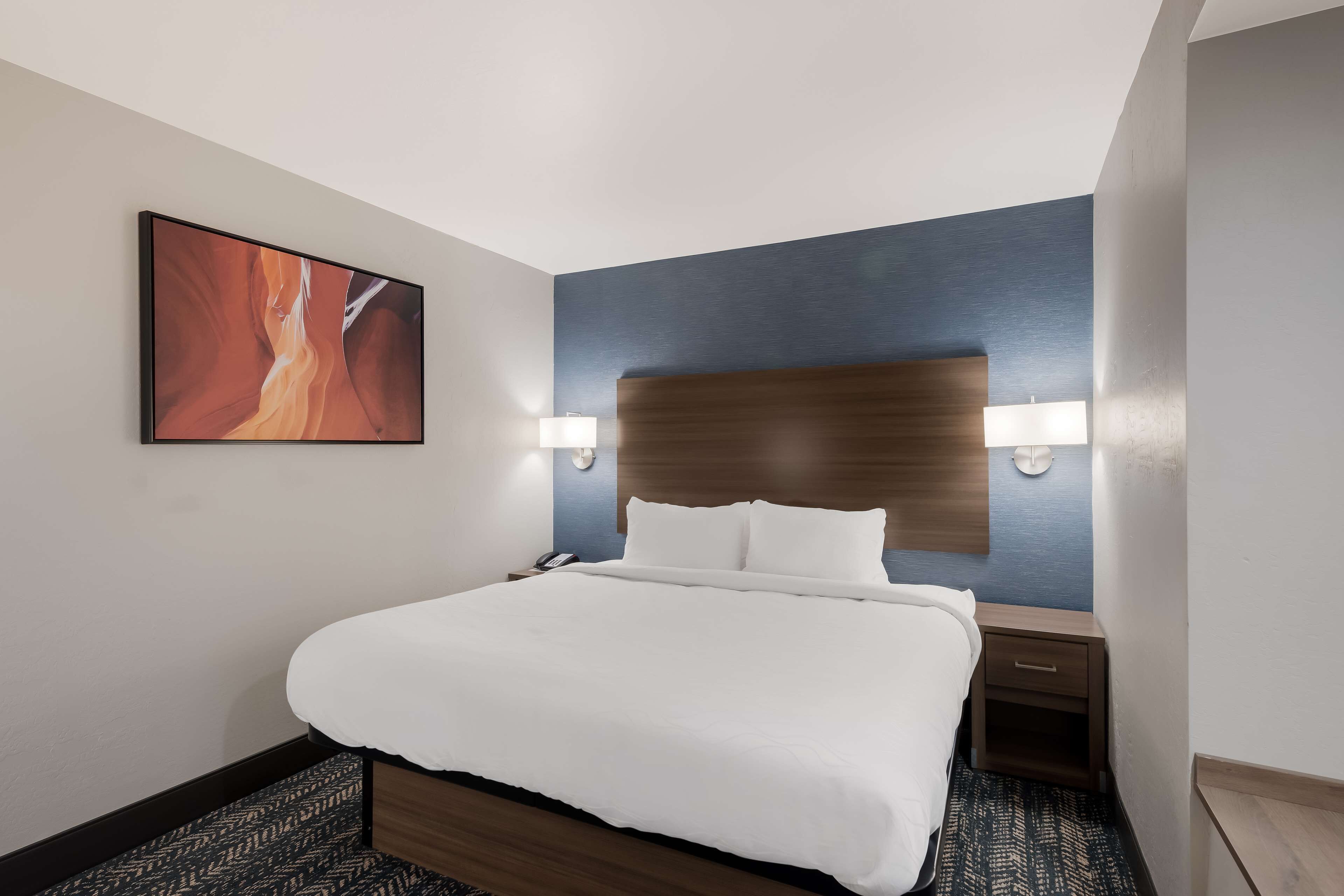 Habitación de hotel con una cama grande, cabecera, lámparas de noche, teléfono y un cuadro en la pared.