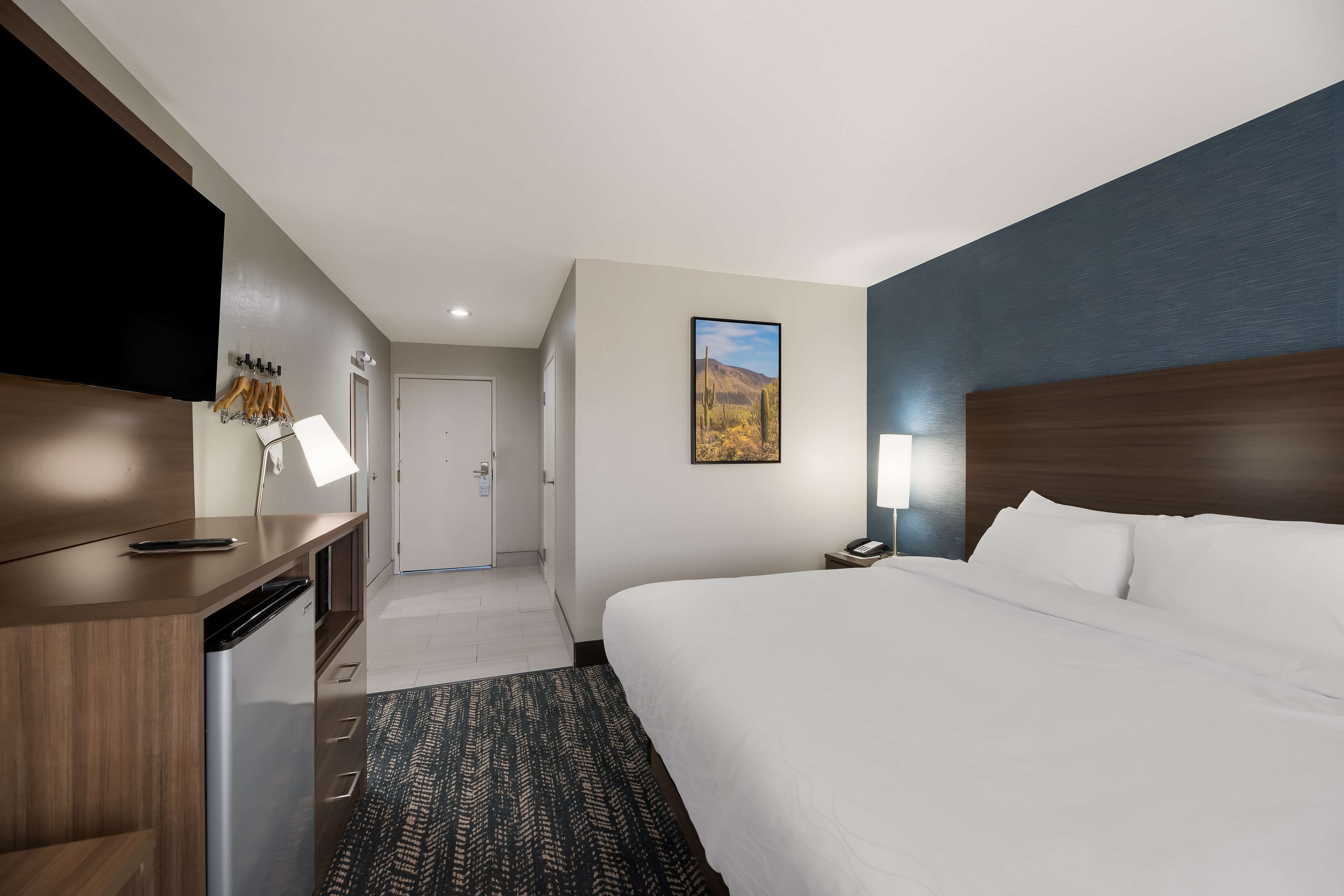 Une chambre d’hôtel comprenant un lit, un bureau avec un téléphone et une lampe, un téléviseur fixé au mur, et une porte donnant accès à une salle de bain.