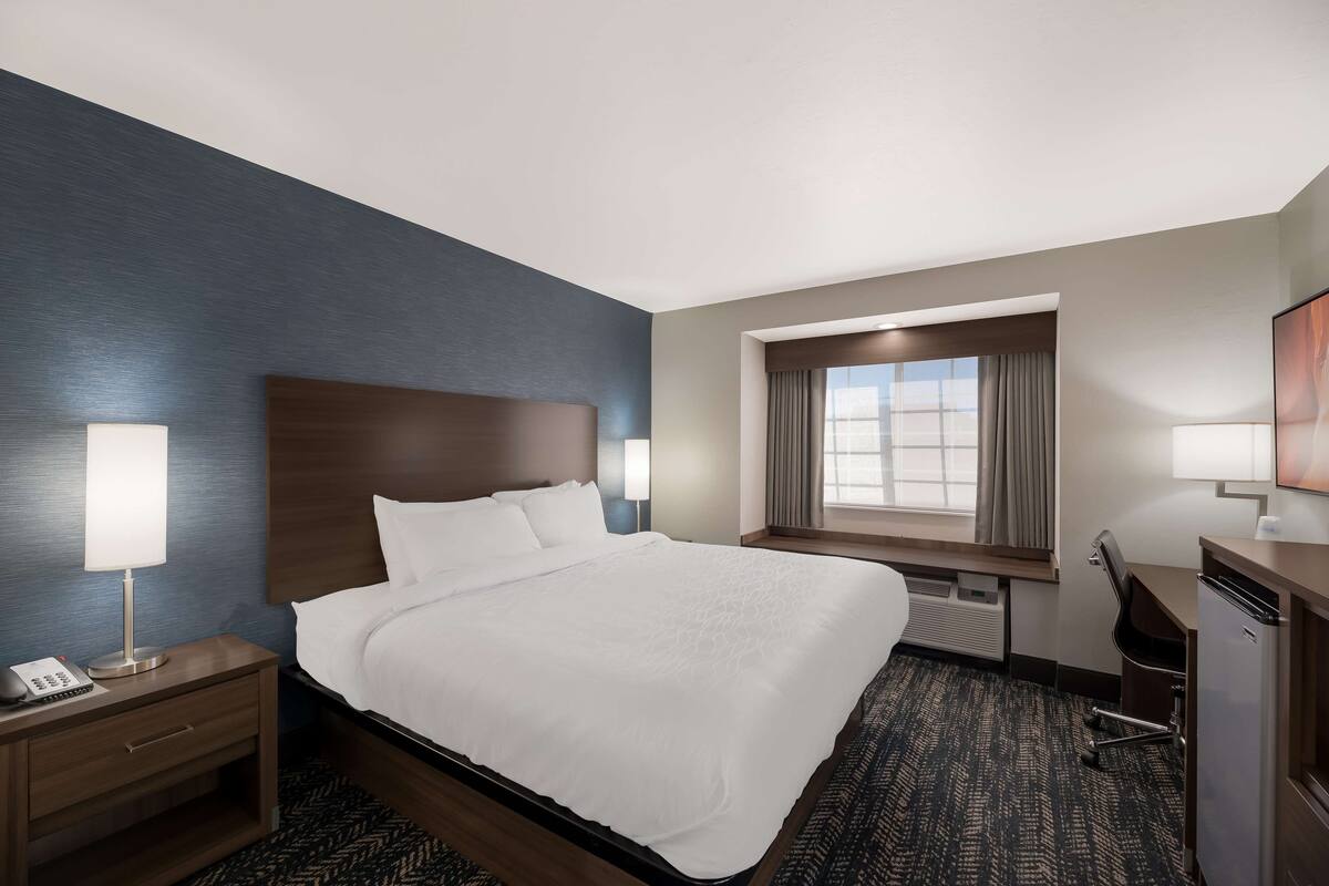 A hotel room with a large bed, a desk, a chair, a lamp, and a window with curtains.