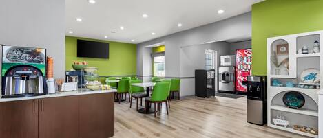 A modern kitchen with a coffee station, green chairs, and a white refrigerator.