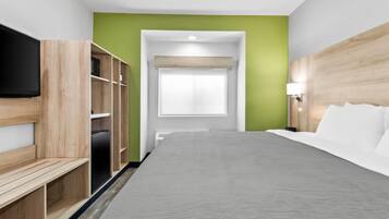Habitación de hotel con cama, televisor, estanterías de madera, pared de acento verde y una ventana.