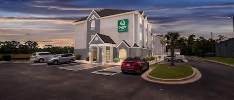 A hotel with a 'Quality Inn' sign, a parking lot with several cars, and a well-maintained lawn area.