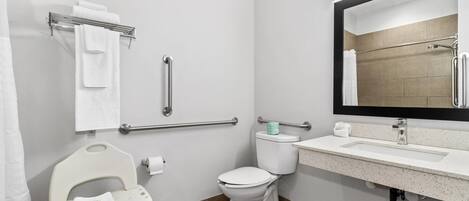 A modern bathroom with a toilet, sink, and handrails.