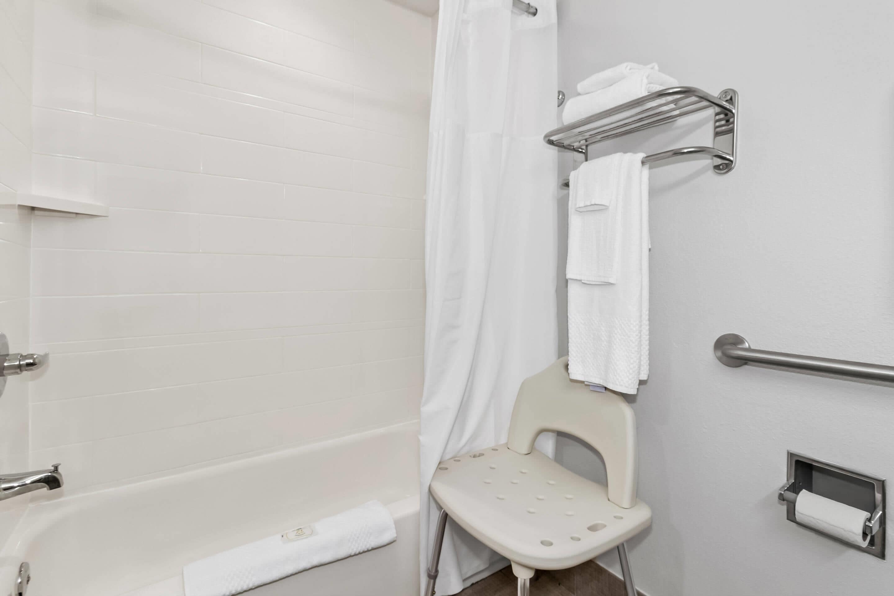 Une salle de bain avec une baignoire blanche, un rideau de douche, une barre d’appui, des toilettes et un porte-serviettes.