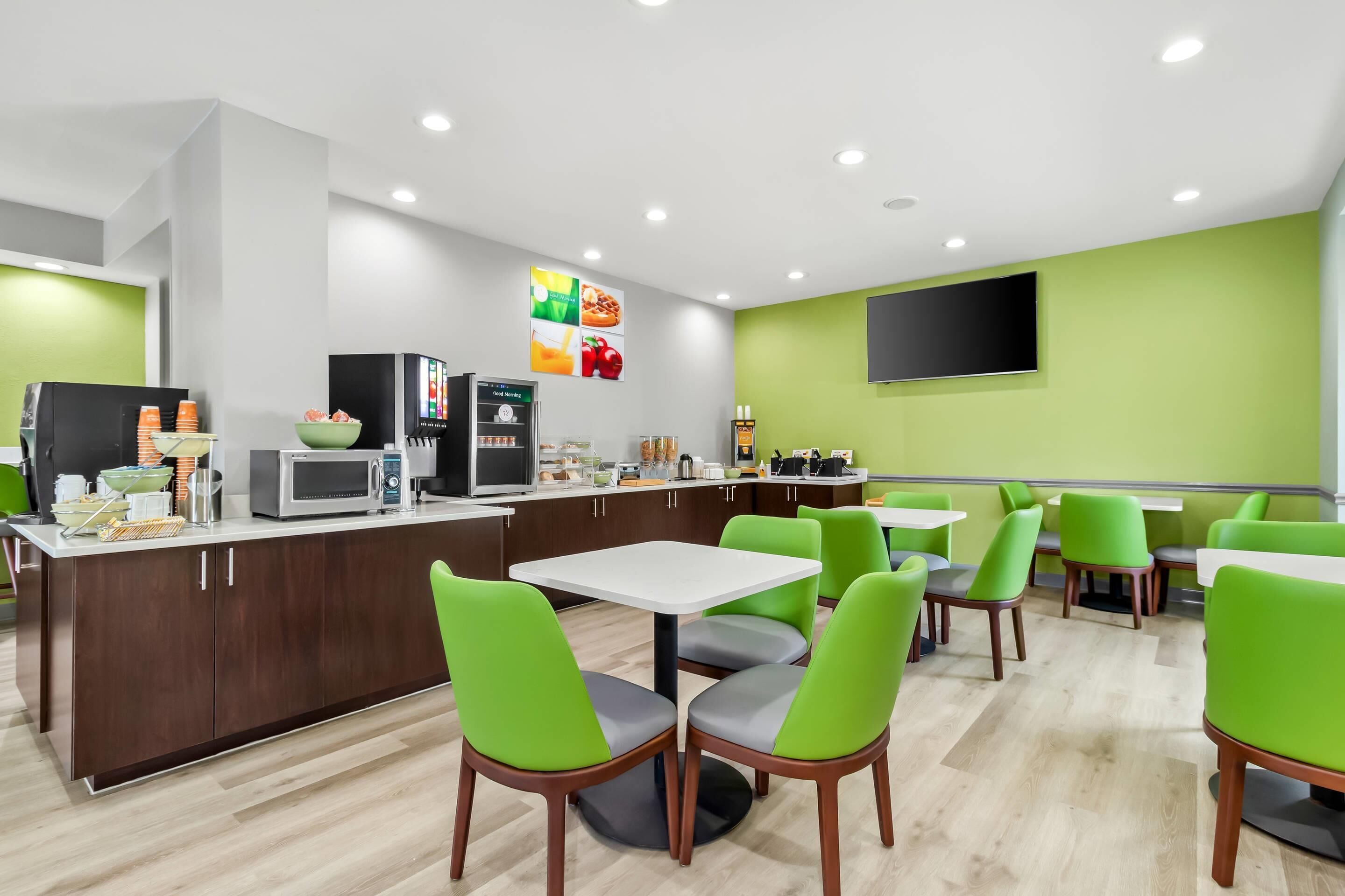 A modern restaurant with green chairs and white tables, a microwave, and a refrigerator on the counter.