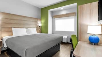 A modern hotel room with a bed, a desk with a lamp, and a window.