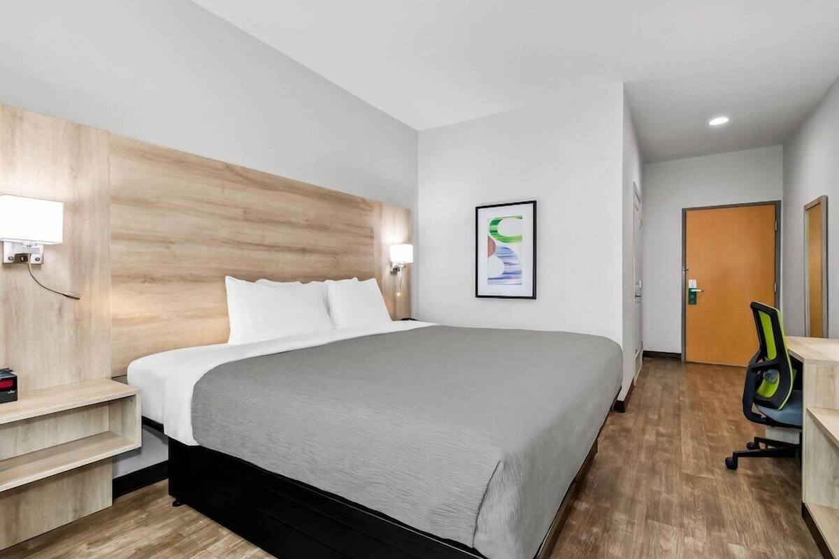 Ein Hotelzimmer mit Bett, Nachttisch, Wandlampe und einer Tür.