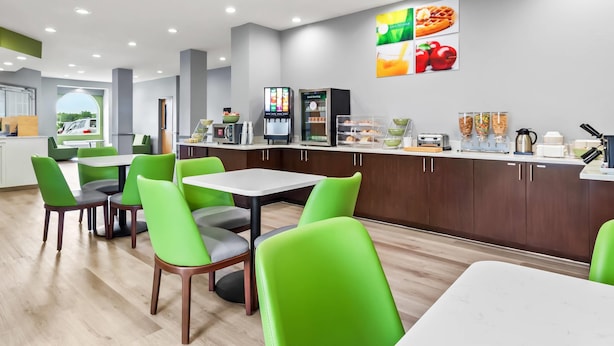 A modern cafe with green chairs and tables, a coffee machine, and a menu board. - Quality Inn Shallotte near Ocean Isle Beach (Shallotte)