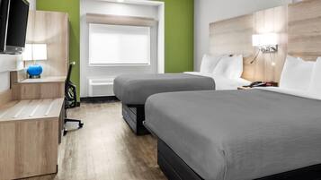 A hotel room with two beds, a desk, a TV, and a window with blinds.